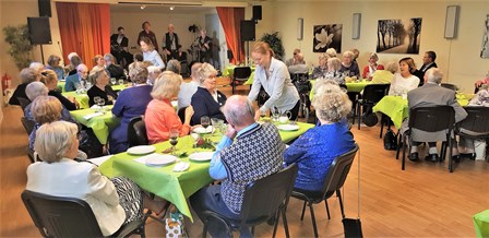 Stor lokal med många dukade bord bär medlemmarna lyssnar på en orkester