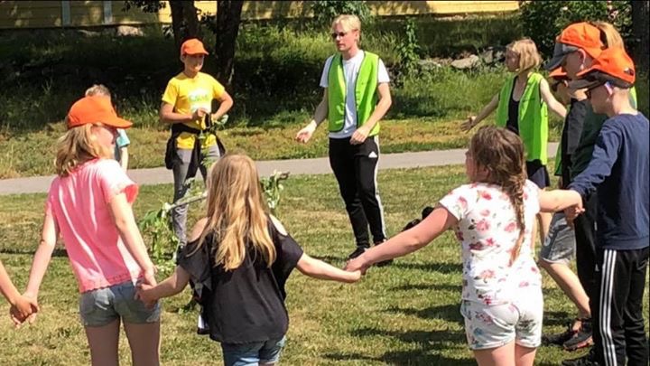 Deltagare och ledare dansar i ring runt midsommarstången.