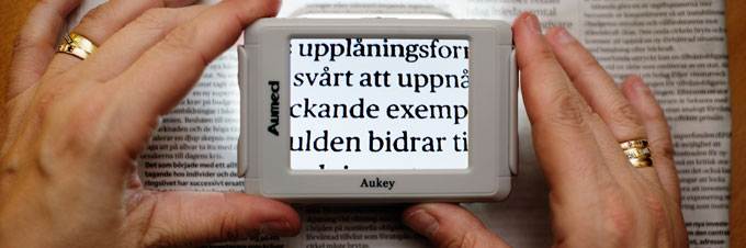 Ett par händer håller i ett förstoringsglas som förstorar en text.